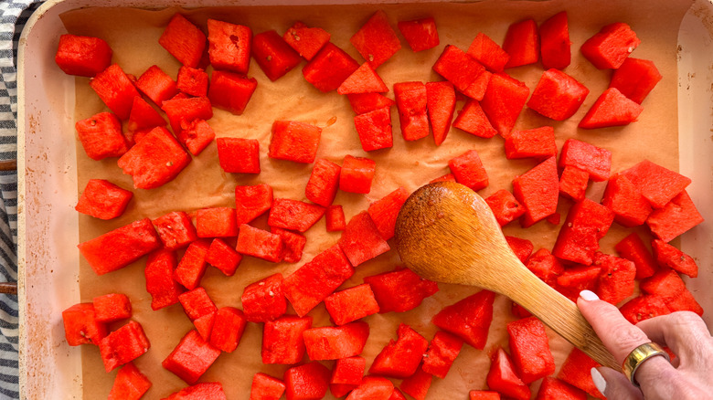 wooden spoon spreading watermelon chunks on sheet pan