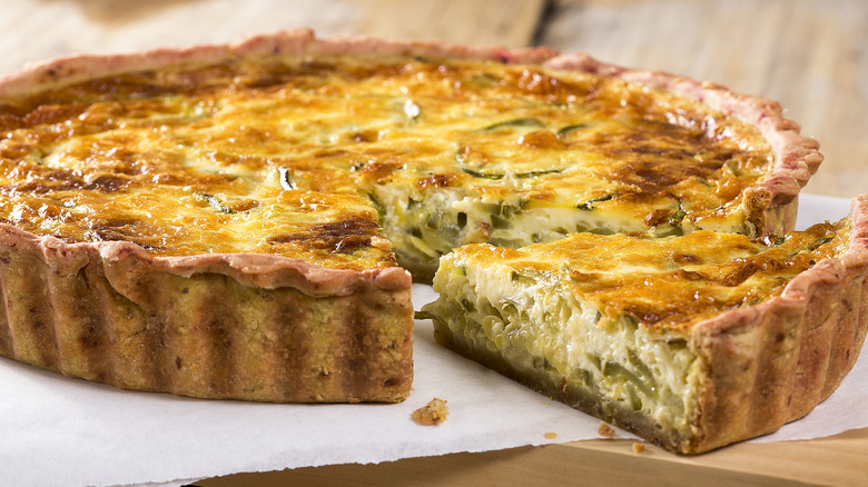 A vegetable quiche with a wedge sliced out of it