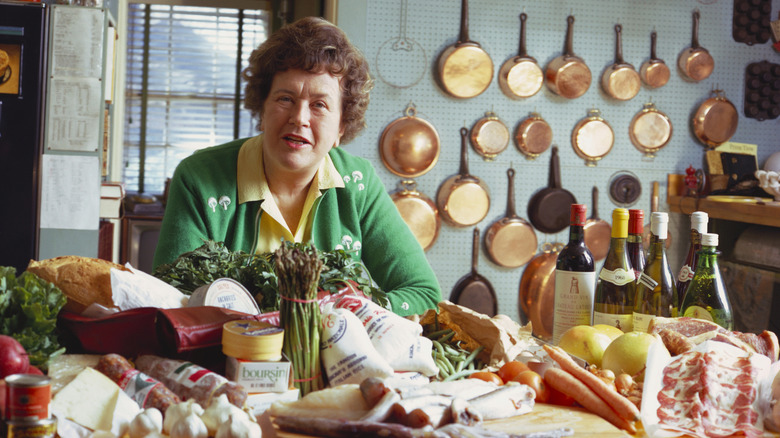 Cookbook author and TV host Julia Child poses before an array of food and wine in her kitchen