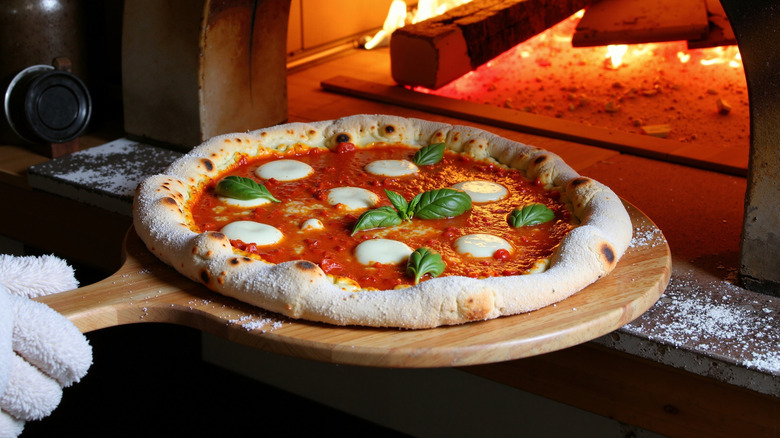 A person transferring a homemade pizza into a pizza oven using a wooden pizza peel