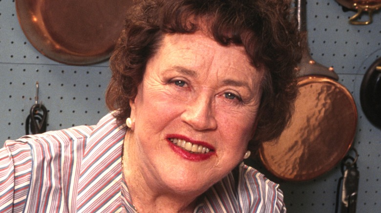 Julia Child smiling in front of copper pots hung up on back wall