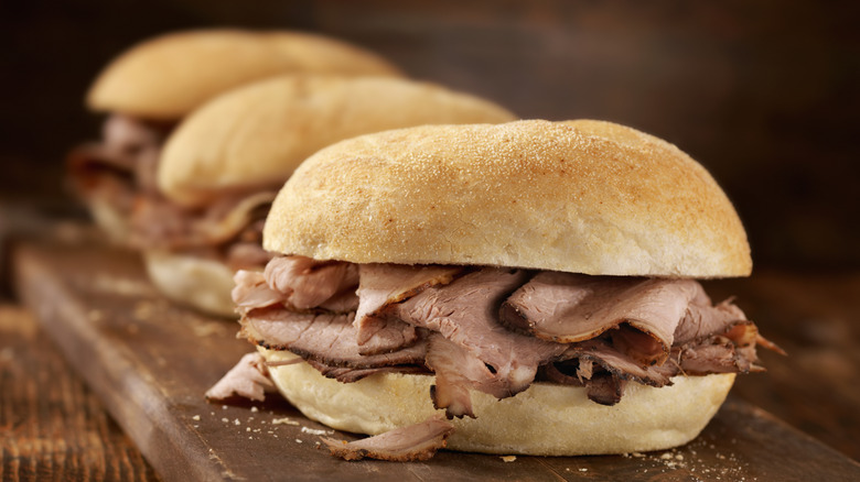 Three roast beef sandwiches on a wood board