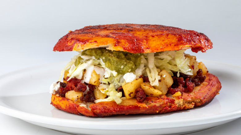 Pambazo Mexican sandwich with chorizo, potatoes, lettuce, and green salsa on a white plate