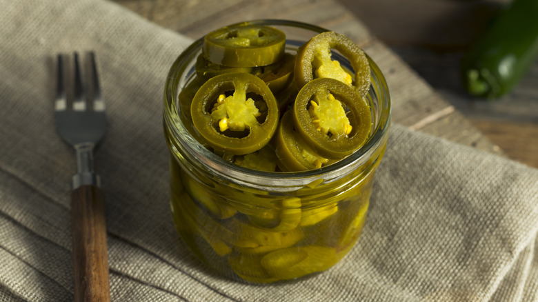 A jar of pickled jalapeños on a table cloth.