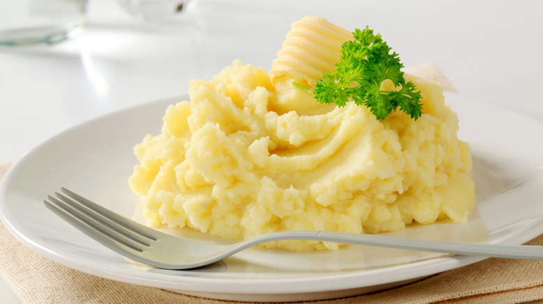 a mound of mashed potatoes topped with butter and parsley sit on a white plate with a fork sitting beside it