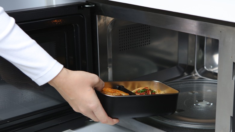 Hand placing dish of food into microwave