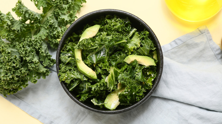 kale and avocado in a black bowl with more kale and a linen on the table.