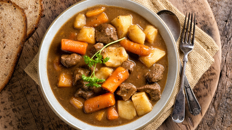 Bowl of steak soup with utensils and bread beside it