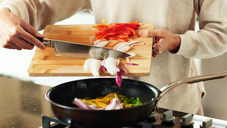A person using a knife to push onions off of a cutting board and into a pan