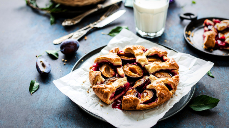 table set with sliverare, milk glass, plum pastry on parchment paper lined plate