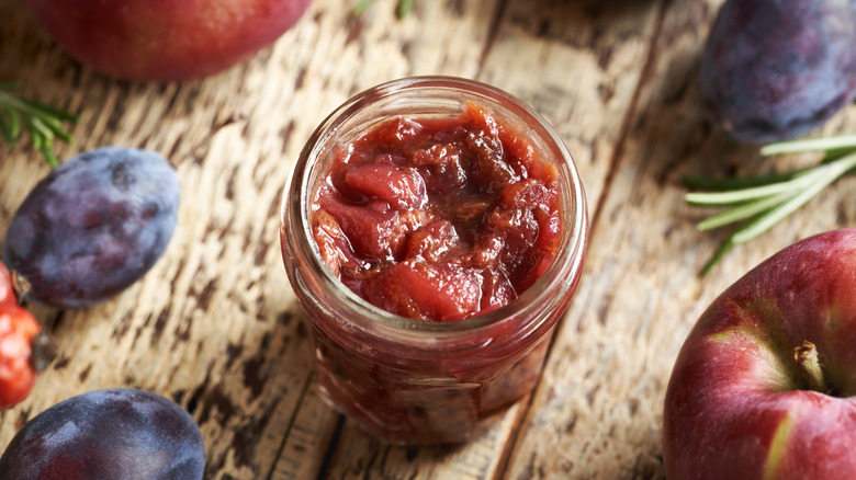 jar of plum jam opened with whole plums on wooden background