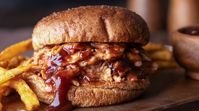Barbecue sauce oozes out of tender pulled pork sandwich with fries on the side