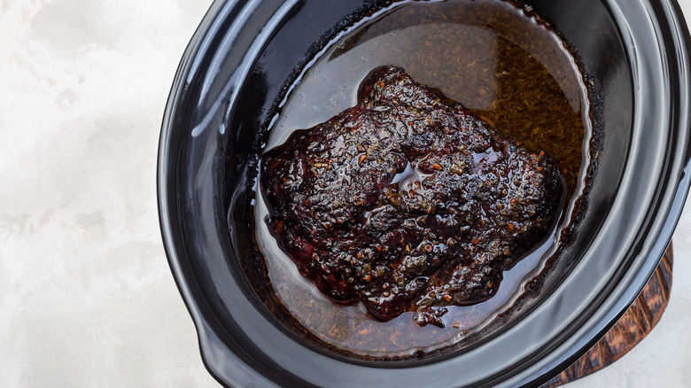 A pork shoulder surrounded by braising liquid in a slow cooker
