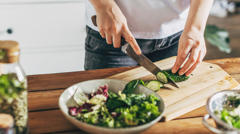 Woman cutting a cucumber with a knife while making a salad