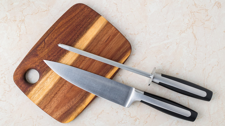 A knife and honing rod resting on a wooden cutting board