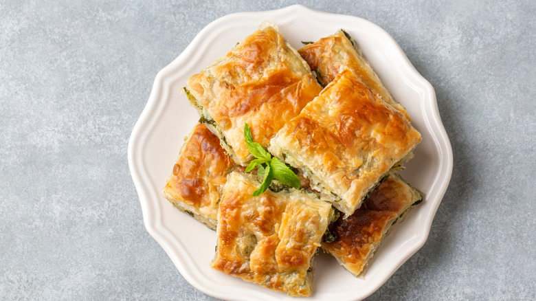 scalloped white plate with stacked with flaky Spanakopita slices