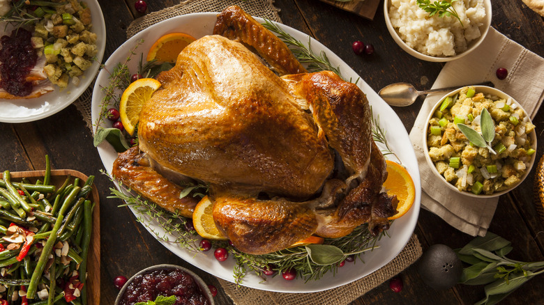 A beautifully crisp roasted turkey on a bed of greens and oranges on a table full of festive dishes