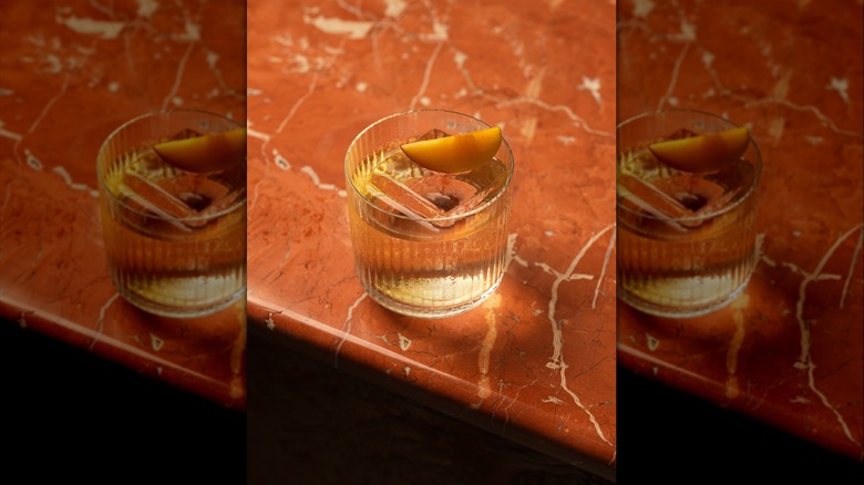 Overhead view of a bourbon cocktail with peach garnish on a bar table