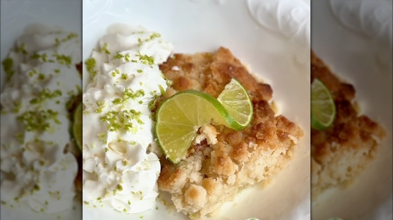 Slice of key lime pie inspired dump cake with crumb topping, lime slice, and whipped cream with lime zest