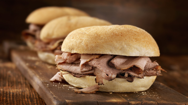 A sandwich made with thin slices of roast beef on a bun with two more out of focus in the background