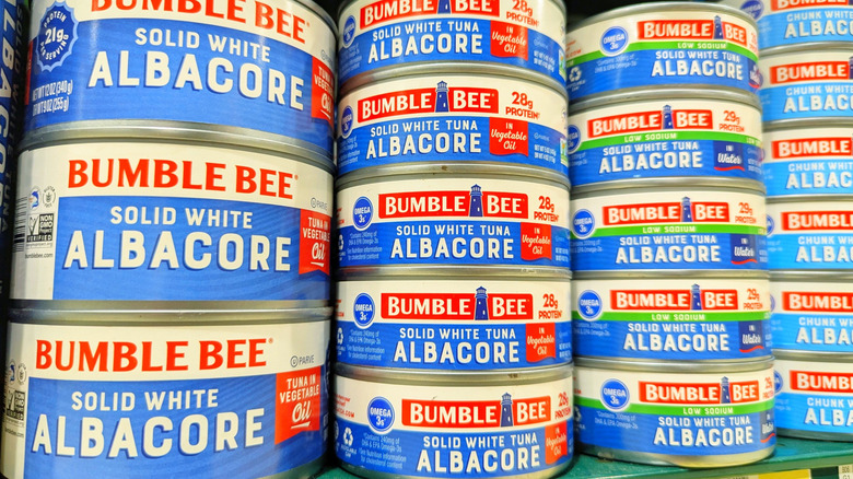 Stacked cans of Bumble Bee white albacore tuna with blue and red labels on a grocery store shelf.