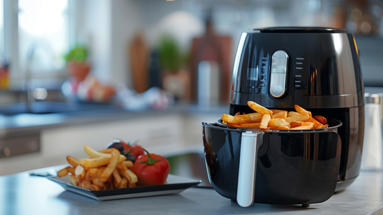 A black air fryer with french fries on a marble kitchen countertop