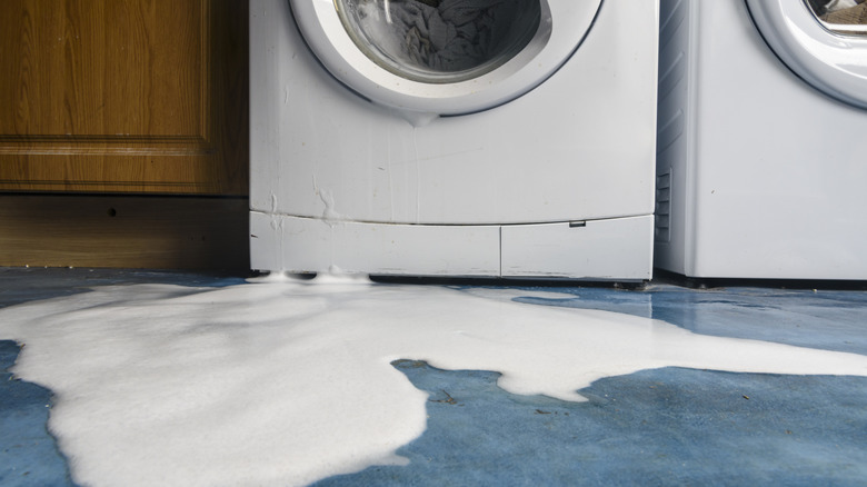 A washing machine with foam leaking out on to a blue floor