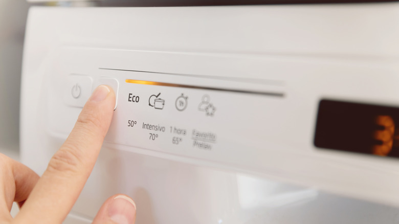 A finger pressing a button on a dishwasher with an eco sign