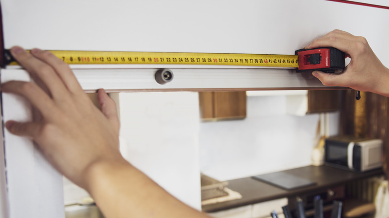 A man measuring cabinets in a kitchen with a tape measure