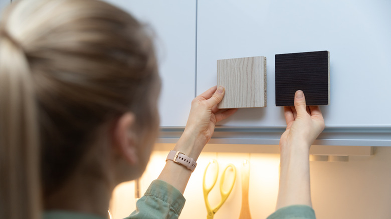 Woman holding two color samples up to kitchen cabinet