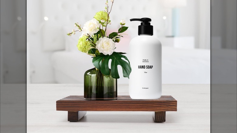 Bottle of hand soap and green vase of flowers on wooden soap tray