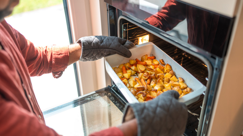 A man putting a dish of potatoes in the oven to keep them warm