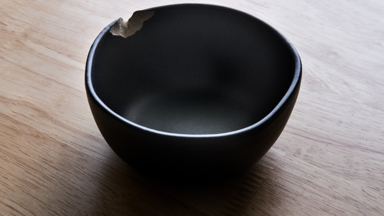 A small, chipped black ceramic bowl on wood surface.