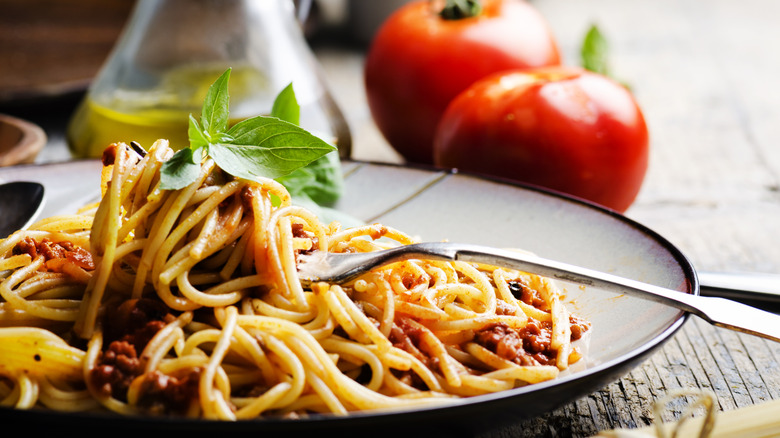 Italian spaghetti in a bowl with a fork beside tomatoes and olive oil