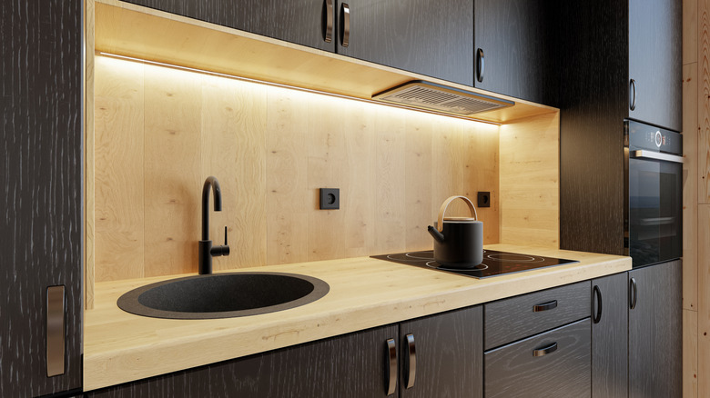 Beautiful task lighting in a modern kitchen with woodgrain cabinets, counters, and backsplash