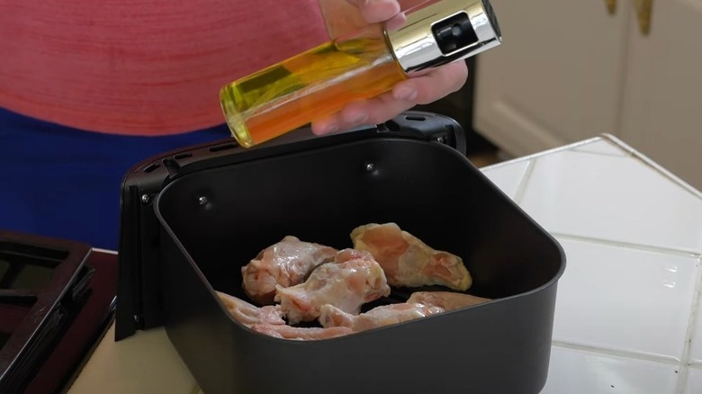 Holding oil sprayer over air fryer basket with chicken