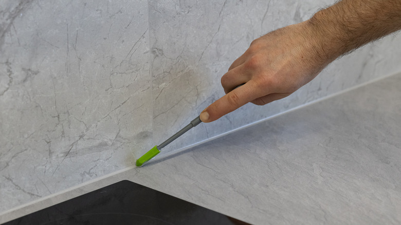 tradesman's arm, using a rounded-tip tool to smooth the seal between a marble countertop and backsplash
