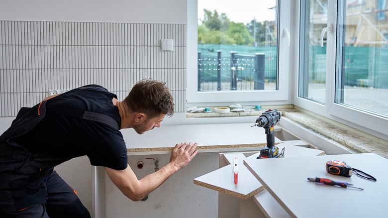 A young tradesman in dark clothing, installing lower cabinets and countertop