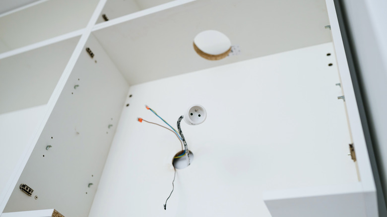 a close-up image of white-box prefabricated cabinetry in mid-installation, with cut-outs for the vent pipe, and wiring pulled for the hood vent's light and its power connections