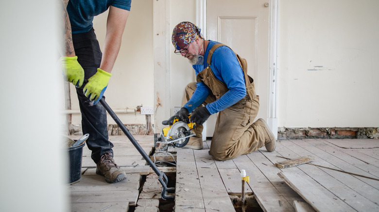 two male tradesmen removing planks from a damaged subfloor in the kitchen of an older home