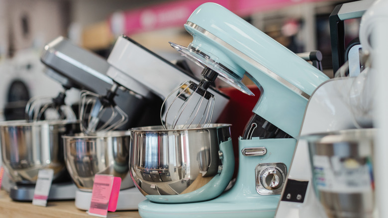 Kitchen stand mixers lined on a store shelf.