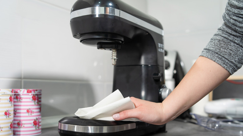 person wiping down a stand mixer with a paper towel