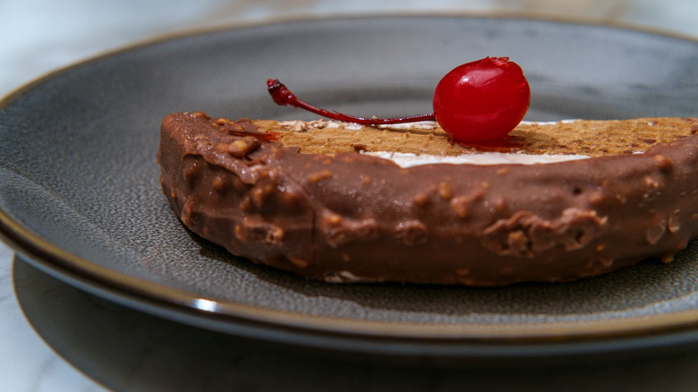 a choco taco sits on a plate topped with a maraschino cherry