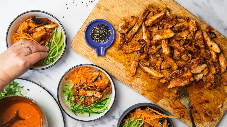 Assembling three Korean BBQ chicken rice bowls.
