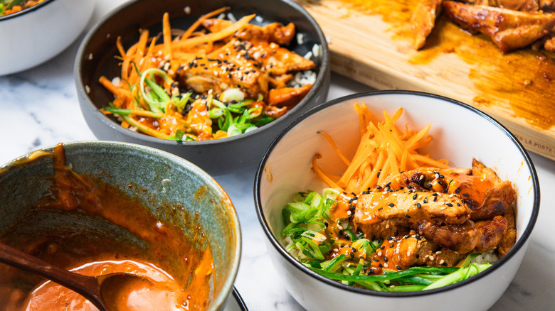 Assembling three Korean BBQ chicken rice bowls.