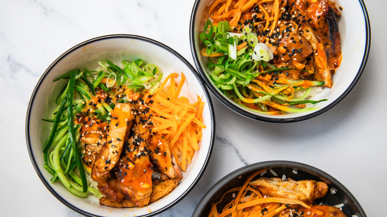 Overhead view of three Korean BBQ chicken rice bowls.