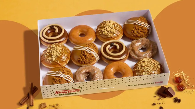 A box of autumnal donuts against an orange, fall-themed backdrop.