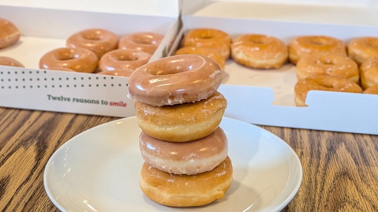 Donuts from Krispy Kreme and Dunkin' stacked on top of each other in front of two open donut boxes