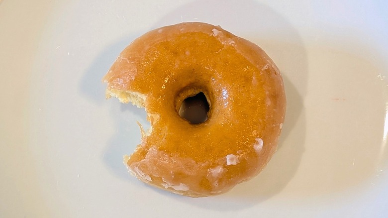 A Dunkin' glazed donut with a bite taken out on a white plate