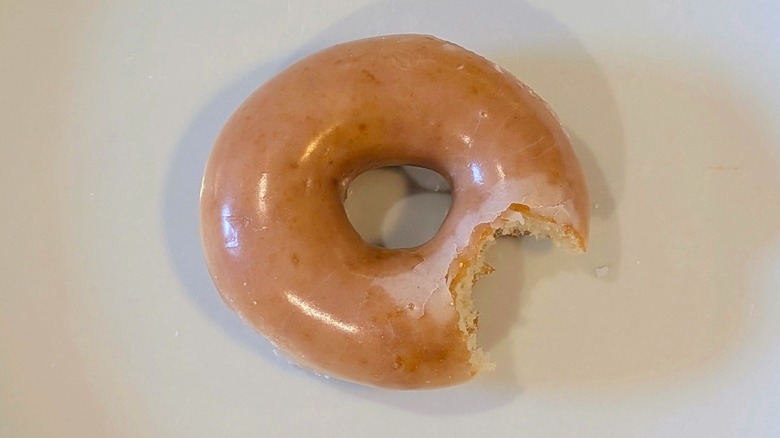 A Krispy Kreme donut with a bite taken out on a white plate